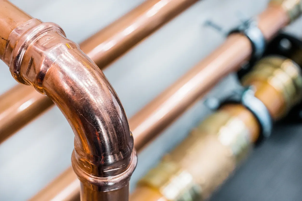 A close-up of copper pipes with a focus on a curved joint. The pipes are shiny and appear to be part of an industrial plumbing system.