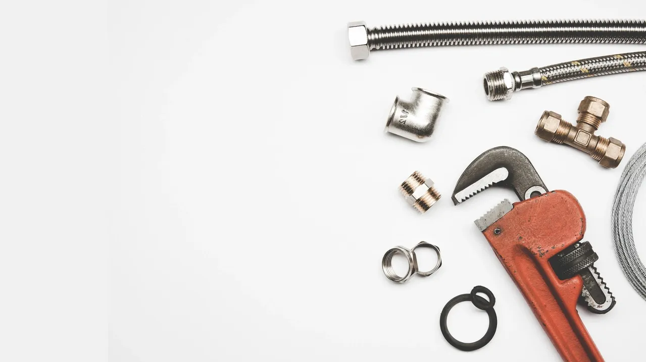 A plumbing wrench, metal fittings, couplings, clamps, and a flexible hose are arranged on a white background.