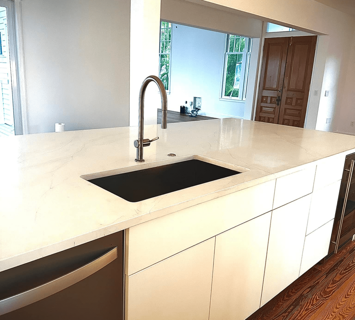 Modern kitchen with white cabinets, a glossy marble countertop, a stainless steel sink, and a sleek faucet. Bright natural light from windows enhances the space.