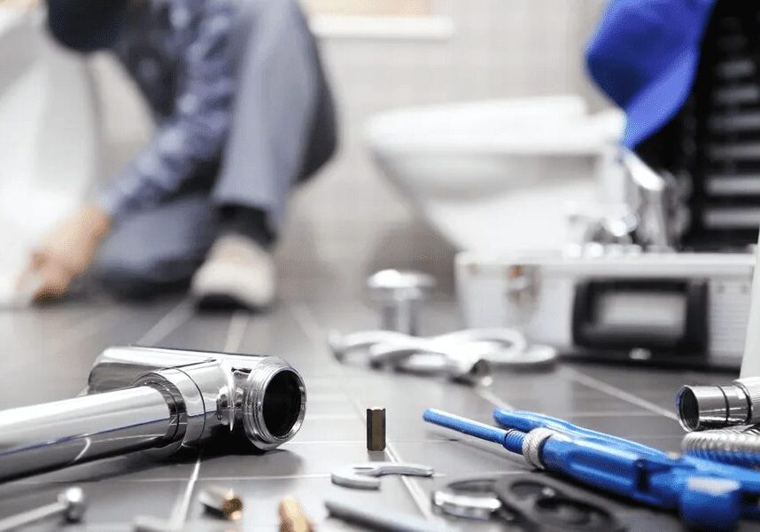 1 Plumber working on a toilet installation, surrounded by various tools and parts on a bathroom floor.