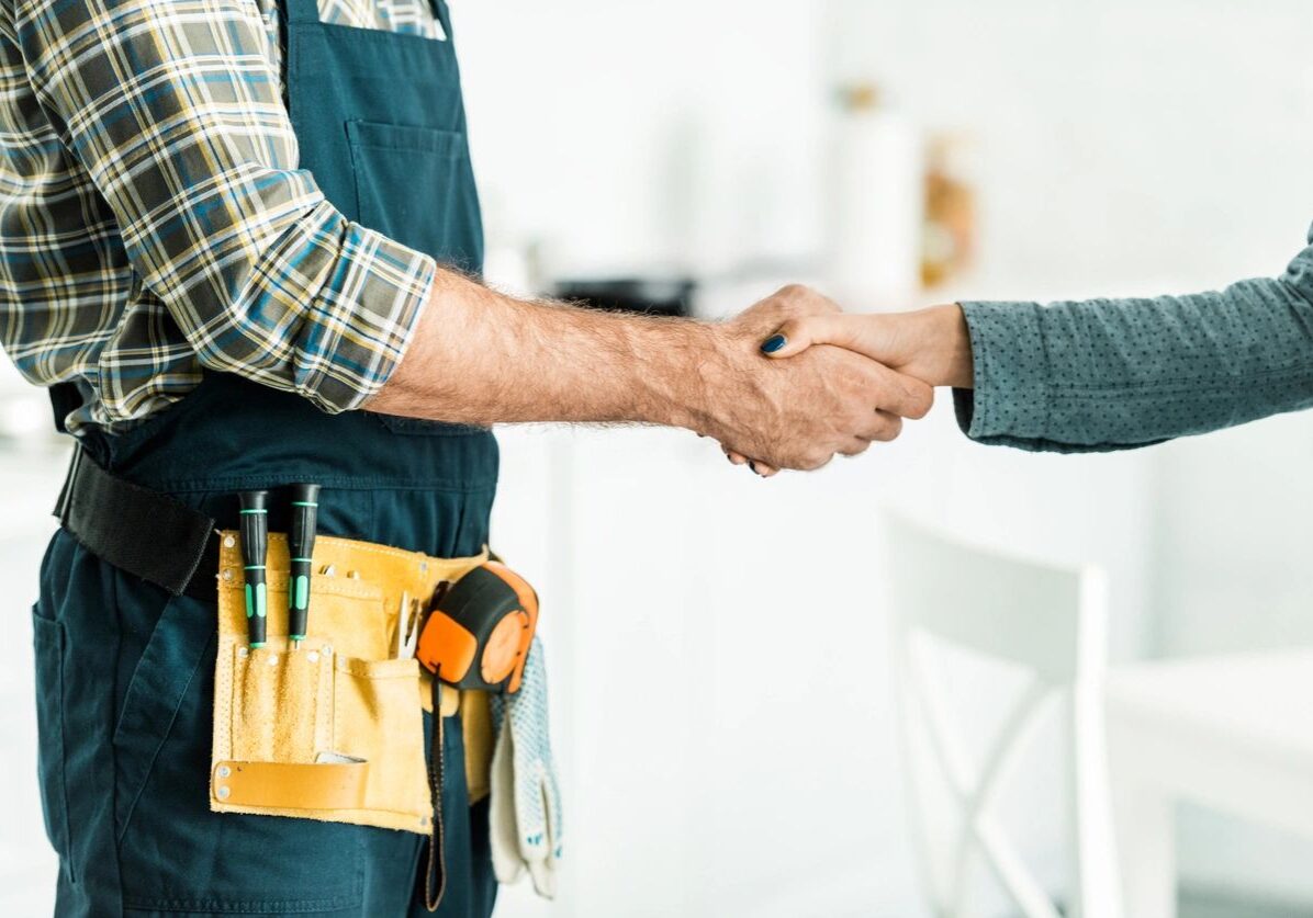 1740473456860_IMAGE-50265_20_2821_29 A person in a plaid shirt and tool belt shakes hands with another person in a gray sweater.