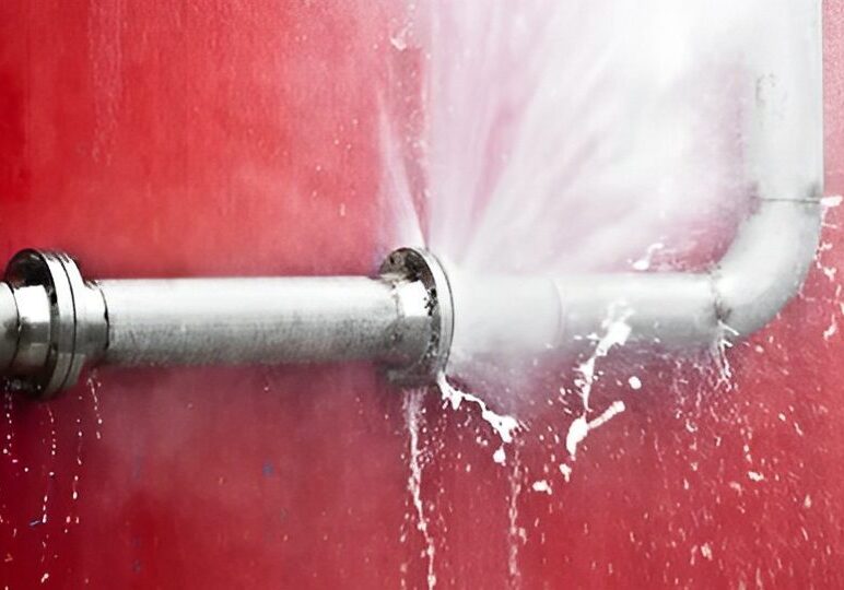 fc279eb4-2d41-4d52-bdd9-092cb72bdba8 Water spraying from a burst pipe against a red background.